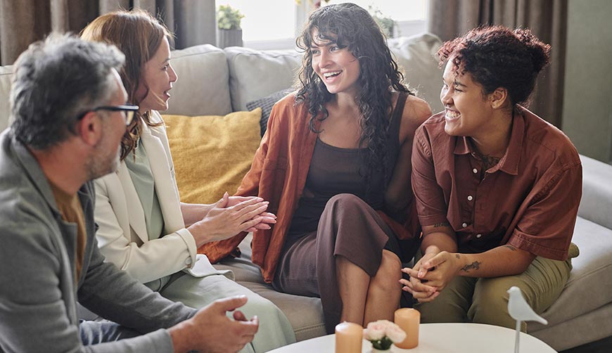 A group of people sit around a table on soft chairs. They are in discussion.
